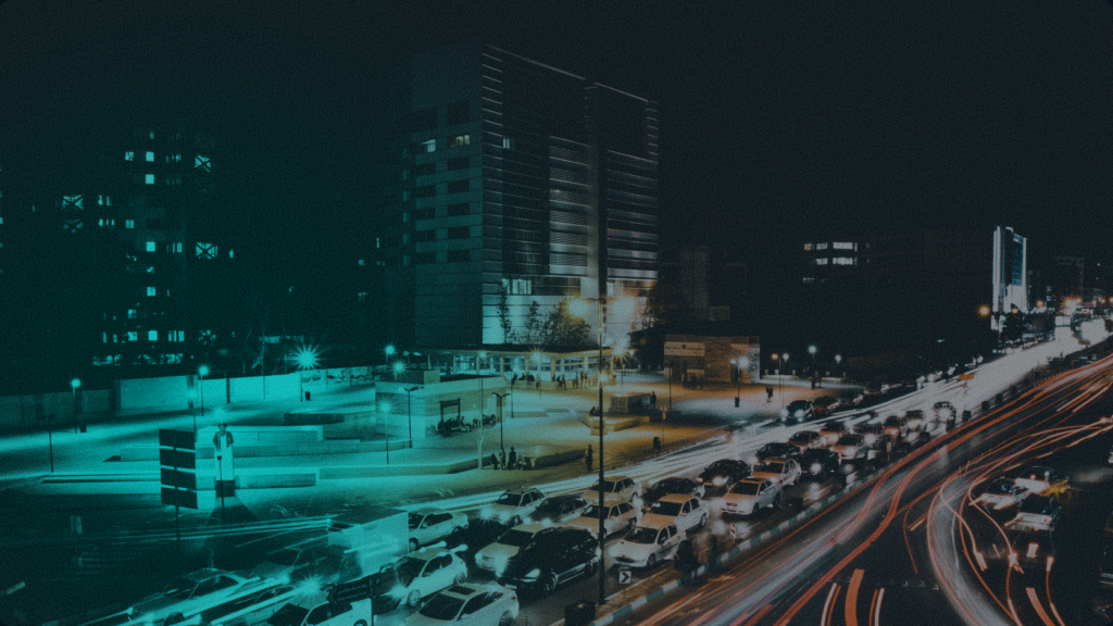 An aerial night view of city traffic lights and modern office buildings under a teal-tinted lens, symbolizing urban liquidity and real-time cross-border financial movement