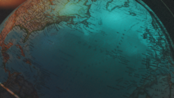 Close-up view of a globe illuminated in teal and warm light showing international cross-border corridors